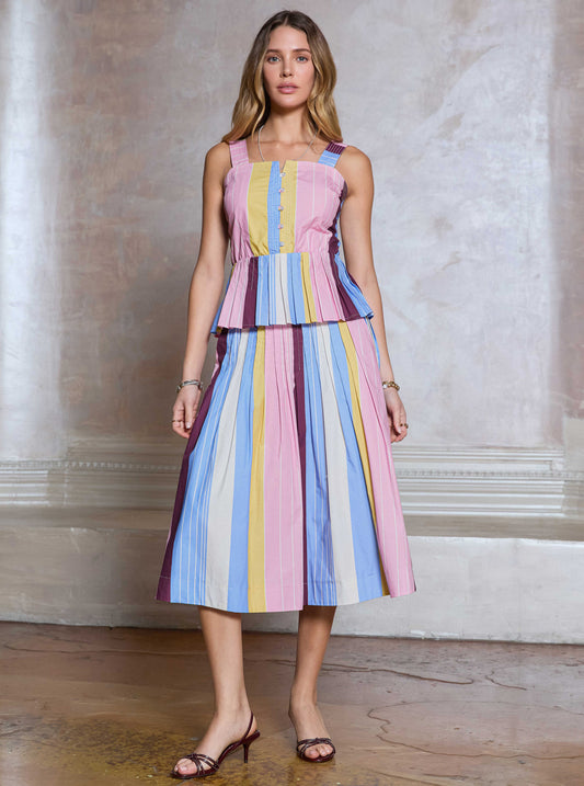 Woman wearing a colorful striped dress standing against a neutral wall.