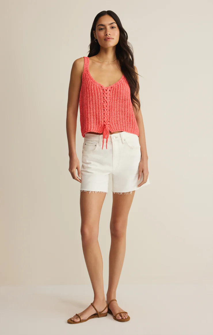 Woman wearing a coral tank top and white shorts on a beige background