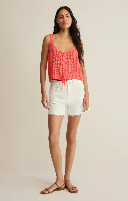 Woman wearing a coral tank top and white shorts on a beige background